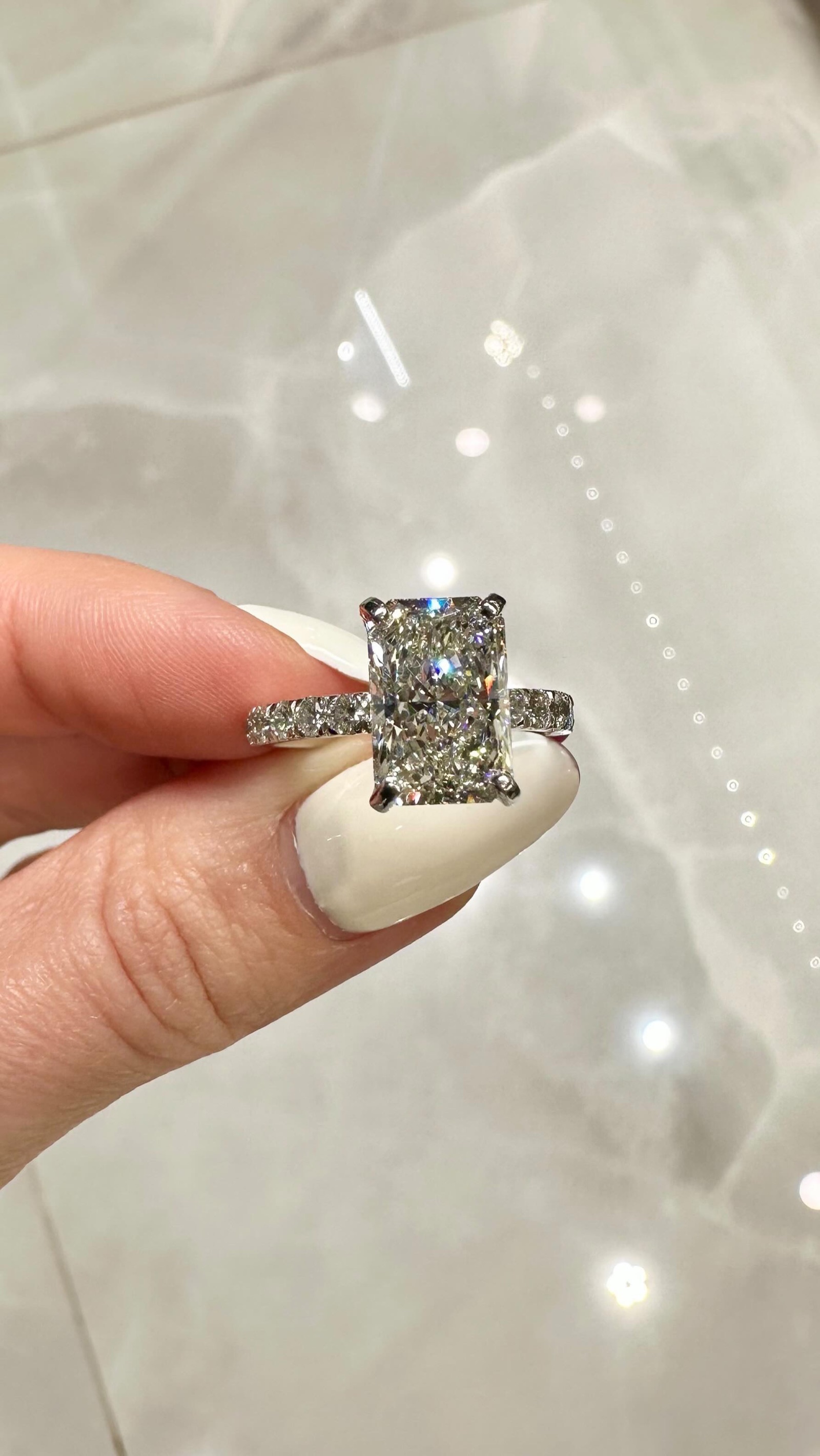 A radiant cut diamond engagement ring held up to the light, from the Mint Jewelers Instagram