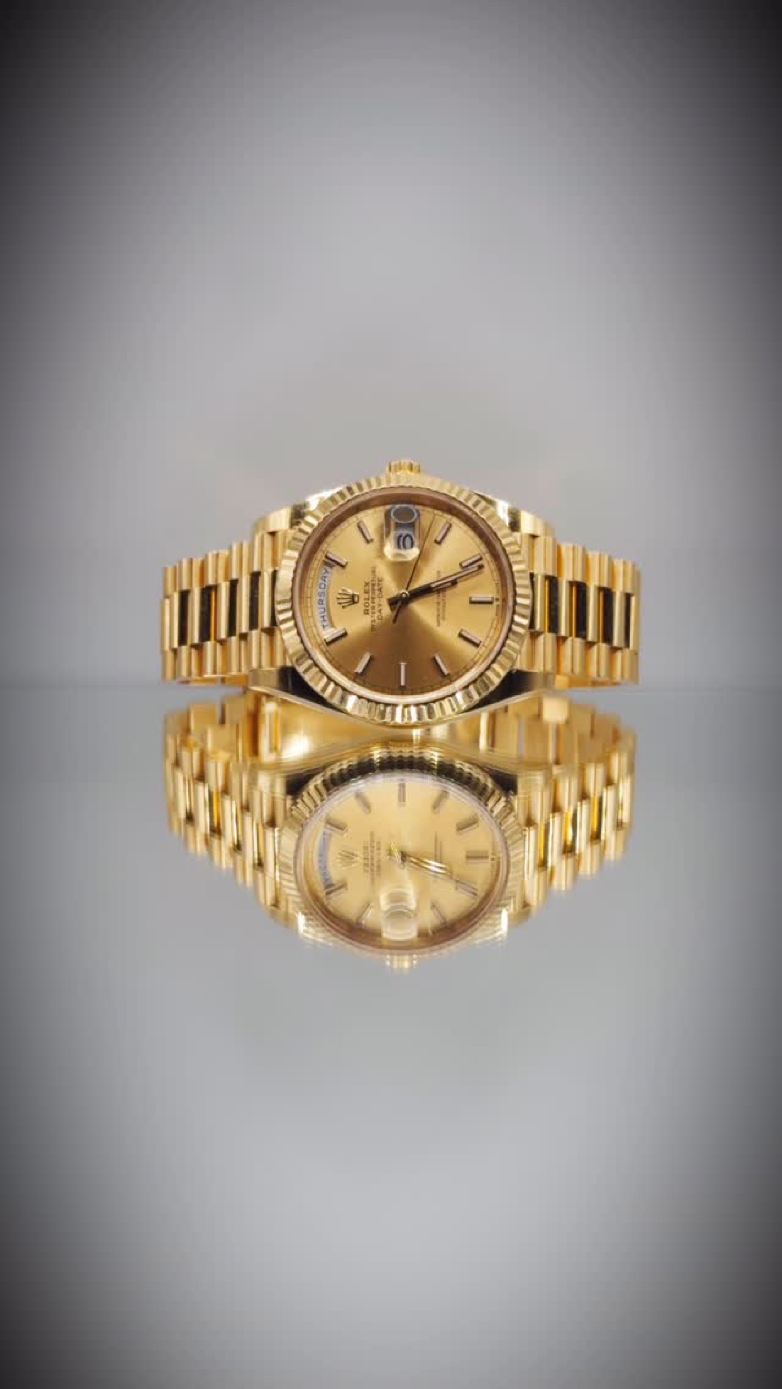 A yellow gold Rolex Day-Date standing on a reflective surface